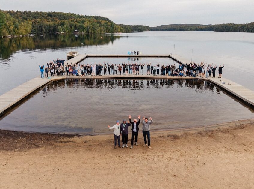 Drone view of reIGNITE conference attendees on a dock with the surrounding lake as a background.